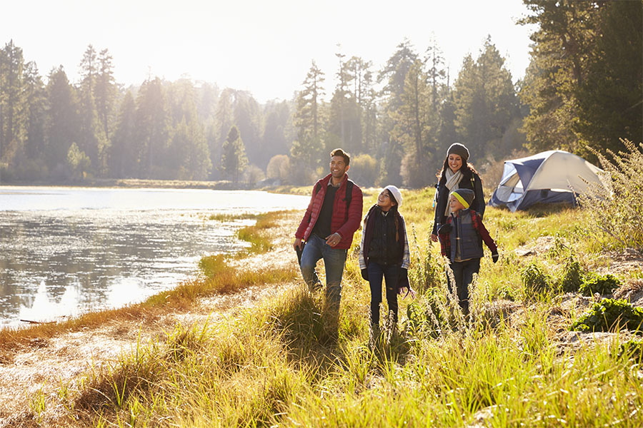 About Our Agency - Parents and Two Children on a Camping Trip Walking near a Lake on a Sunny Day