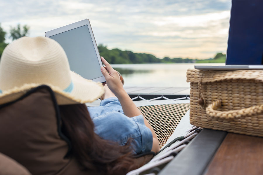 Client Center - Woman with a Laptop and Tablet Working Remotely While on a Hammock and Enjoying a Lake View at Dusk